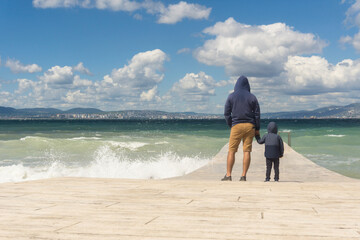 Father and son are standing on the pier, admiring the seascape, raging autumn sea.