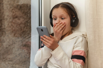 Shocked teenager is surprised using smartphone, headphones. Shocked face. Teen with gadgets. Wow....