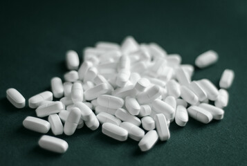 white oblong-shaped tablets lie in  heap on  dark green background.