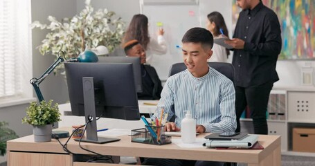 A man of Asian Korean beauty sits in front of an office computer, using a web browser, working in front of a screen, handling the company's social media, creating ads, posts, graphics - Powered by Adobe
