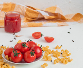 Red cherry tomatoes on a white plate, pasta fusilli, tomato sauce on a white background.