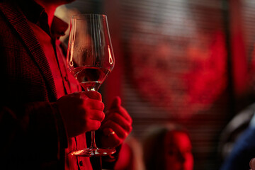 a man beautifully holds a glass of white wine in a red room