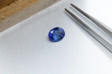 macro mineral faceted stone sapphire with tweezers on a gray background