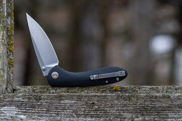 Pocket folding knife with black handle. Knife in a curved position on a wooden window.