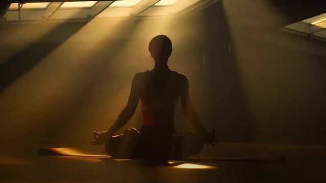 Silhouette of a sporty girl sitting in lotus position on yoga mat under sunlight