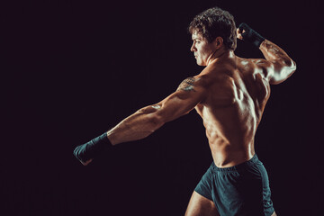 Fototapeta na wymiar Side view of aggressive muscular boxer who strikes isolated on dark background. Sport concept