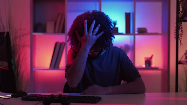 Epic fail. Clueless man. Meme expression. Confused guy showing facepalm gesture with hand feeling disappointed sitting work desk dark neon light room interior looped.