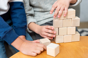 Fototapeta na wymiar Boys play cubes with each other . Two children of different ages are building something with wooden bricks. Hands close up 