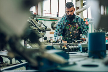 Male worker pressing ink on frame while using the printing machine in a workshop