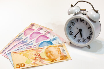 50, 100 and 200 Turkish banknotes and alarm clock on isolated white background. Time is money concept.