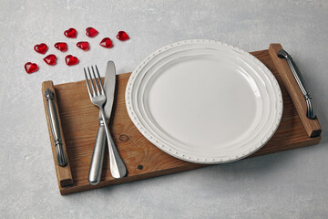 An empty white plate with cutlery on a wooden tray and red caramel hearts