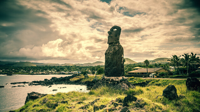 Ein Moai an der K&uuml;ste von Rapa Nui mit Korallenaugen vor dramatischem Himmel