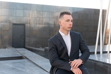 Young handsome stylish man in checkered jacket thoughtfully looking away while sitting outdoor