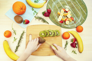 Child's hands are cutting kiwi on cutting board. Preparation of fruit salad. Top view. Flat lay.
