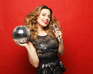 Young blond woman with long wavy hair dressed in evening dress holding a microphone and disco ball