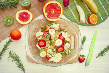 Fruit salad in a plate with sliced strawberries, kiwi, banana, orange and tangerine. Top view. Healthy organic food.