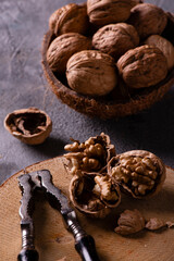 on a wooden disc some kernels in the foreground and an old nutcracker. A bowl with the whole walnuts aside.