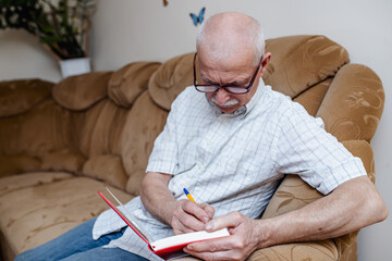 elderly man takes notes in a notebook after paying bills. The old man plans spending and calculates...