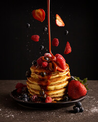 Stack of american pancakes with levitating berries and falling caramel (cajeta). Creative...