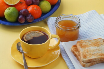 Breakfast - toast bread, tea with lemon, honey in a jar, fruit on a plate. And a beautiful yellow tablecloth.