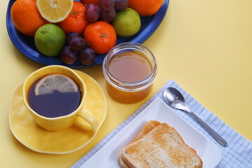 the beautiful yellow color of the tablecloth creates a wonderful mood for a delicious and healthy breakfast - toast, tea, honey, fruits.
