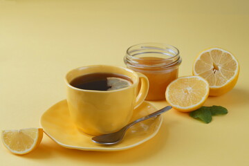 Yellow lemons, tea in a yellow cup, a jar of honey are arranged diagonally. Table background - yellow