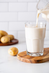 Glass of homemade potato milk with raw potatoes; copy space