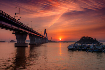 A bridge across the sea and a small fishing boat floating on the sea and the dawn sky
