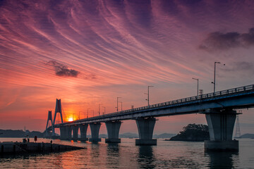 Fototapeta na wymiar A bridge across the sea and a small fishing boat floating on the sea and the dawn sky 