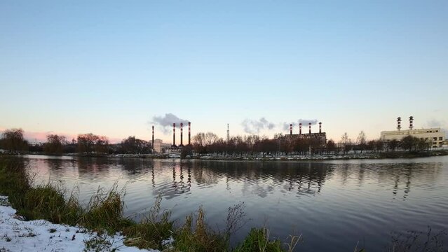 Factory in the middle of a city causing air pollution near water. Thermal power plants in winter. Ecology pollution. Factory pipes thick white smoke steam.