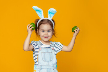 funny happy baby girl with easter eggs and bunny ears on yellow background