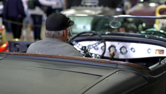 This video shows  rear view of an old man on his phone, sitting in his 1930s hotrod car.