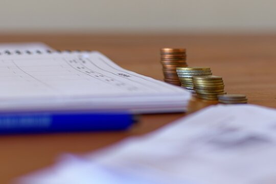 Stacks Of Coins In Front Of A Notebook With A Pen. Concept On Saving Money, Organizing Finances