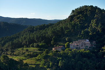 Fototapeta na wymiar Village typique cévenole au pied d'une montagne avec ses cultures en terrasse. Vallée sauvage boisée. France.