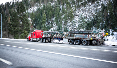 Red big rig semi truck transporting oversized industrial cargo on long flat bed semi trailer...