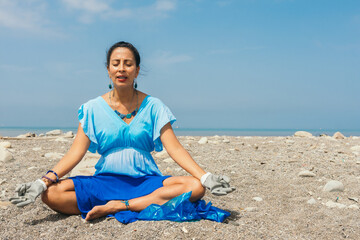 Fototapeta na wymiar A woman meditates on the beach cleansing the energy of the place. An activist meditates with gloves and garbage bag prior to cleaning a polluted beach. Meditation concept