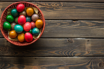 Top view of a red wicker basket with colored Easter eggs on a wooden table