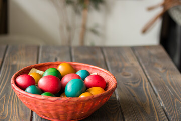 Red wicker basket with colored Easter eggs on a wooden table