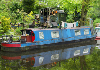 Fototapeta na wymiar an old scruffy blue narrow boat moored next to wooden sheds with washing on the line on the rochdale canal near hebden bridge