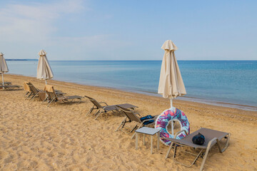 Fototapeta na wymiar Beautiful view of empty sun beds end closed sun umbrellas on sand beach. Greece.
