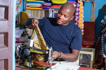 A happy African Nigerian male tailor, fashion designer or business man working with a sewing...