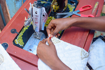 African hands of a female tailor or fashion designer making a dress with a sewing machine in a...