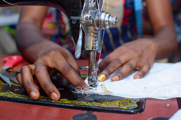 African hands of a female tailor or fashion designer making a dress with a sewing machine in a...