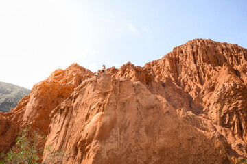 Wide angle view of a caucasian woman sitting on a orange mountain. Sunlight kissed.