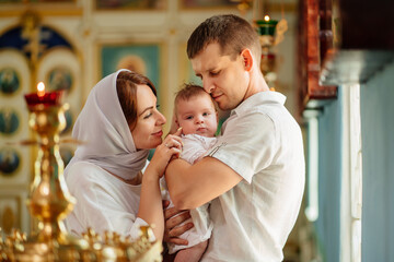 man and woman with baby son in light-colored robes by window in church. 