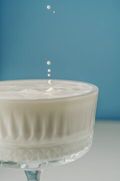 Milk pours into a beautiful crystal glass on a blue background and splashes around.