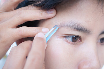 Woman plucking eyebrows with tweezers close up. authentic brown eyes black hair and skin tan asian Thailand. beauty cosmetic concept.