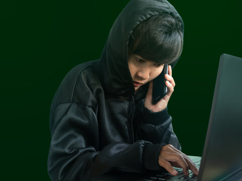 Hacker hooded call mobile phone and typing keyboard laptop computer. hack secret password code system identity theft finance.Unauthorized access to personal data. security technology thief cyber.