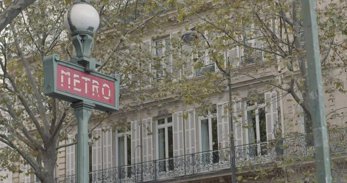 Dolly push in pull back shot of art deco metro sign in Paris with trees, apartments in background