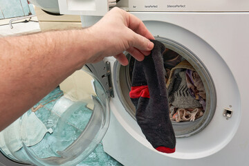 A hand holds a dirty black sock in front of an open washing machine - 485254637